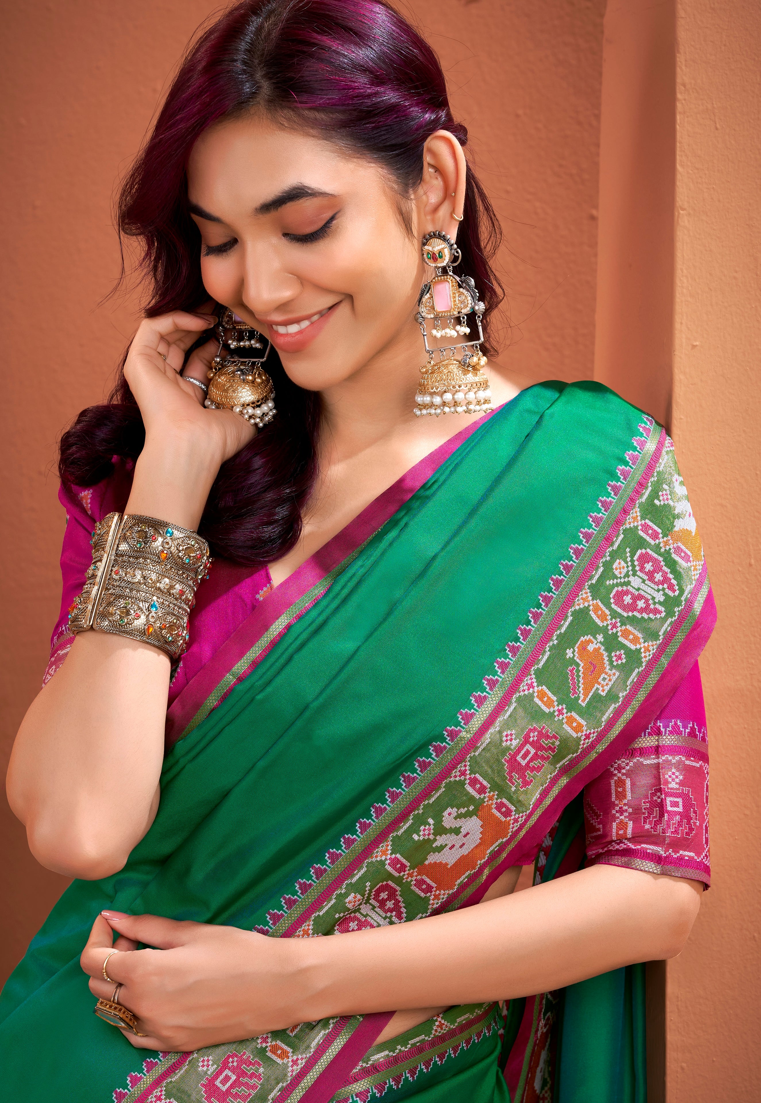 Woman wearing a green and pink saree with jewelry against a brown background