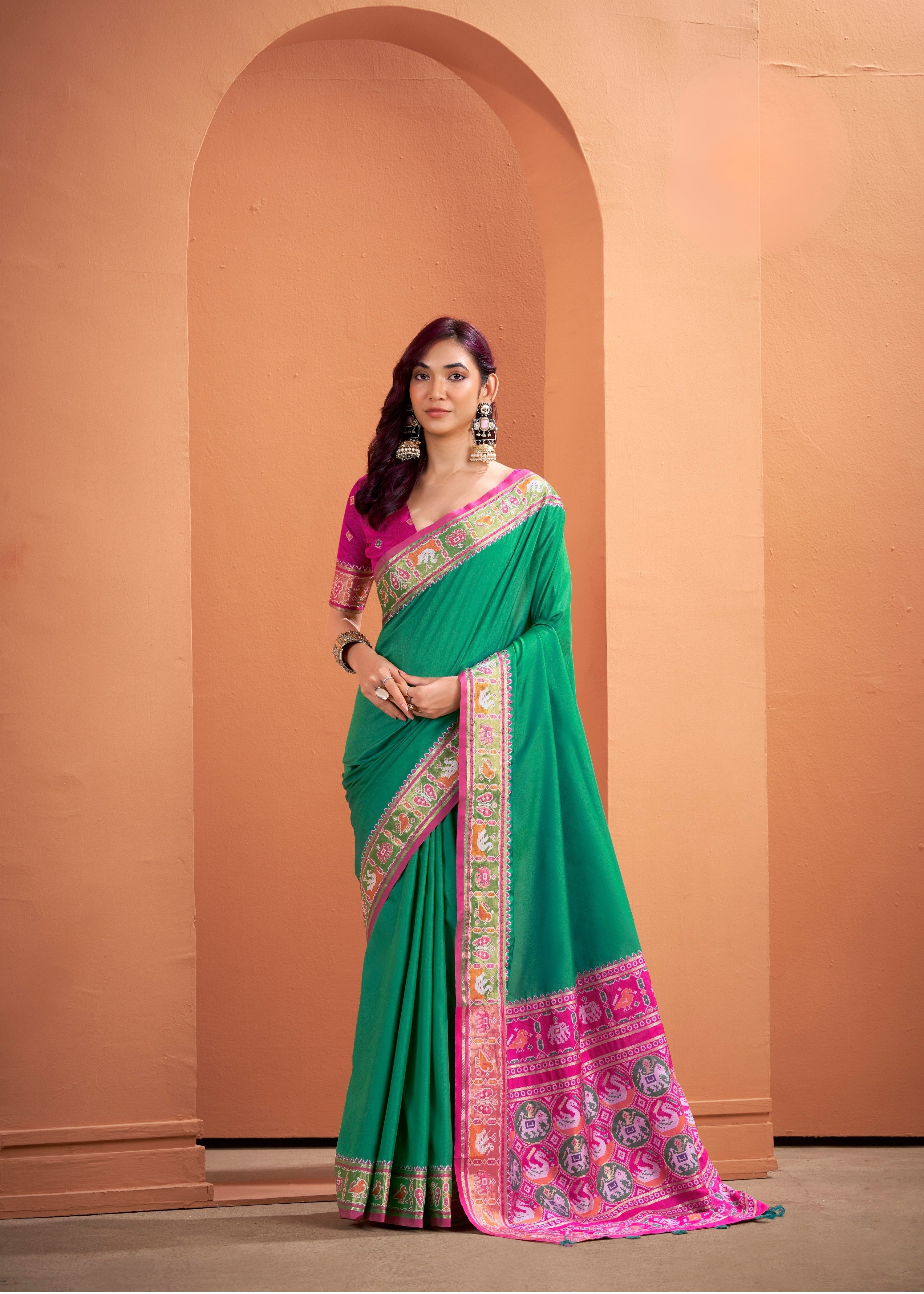 Woman wearing a green and pink saree with a beige wall background