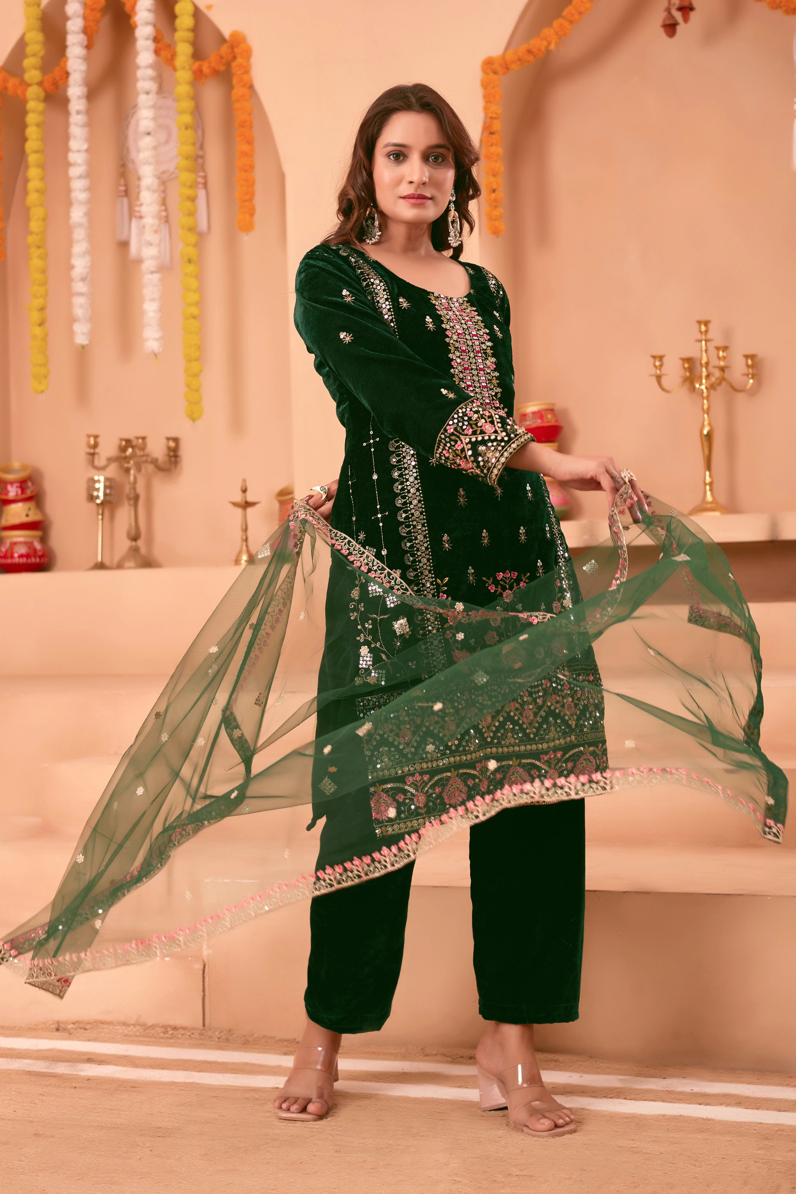 Woman in a green embroidered outfit with a dupatta in a decorated indoor setting