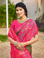 Woman wearing a pink saree with green border and gold jewelry outdoors.