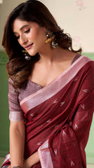 Woman wearing a maroon saree with a white border against a light green background