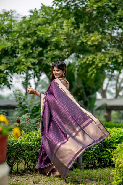 Woman in a deep shade purple saree with zari work posing gracefully in a garden with lush greenery and colorful flowers in the background