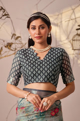Woman wearing a traditional outfit with a patterned blouse and floral skirt, standing against a decorative wall.