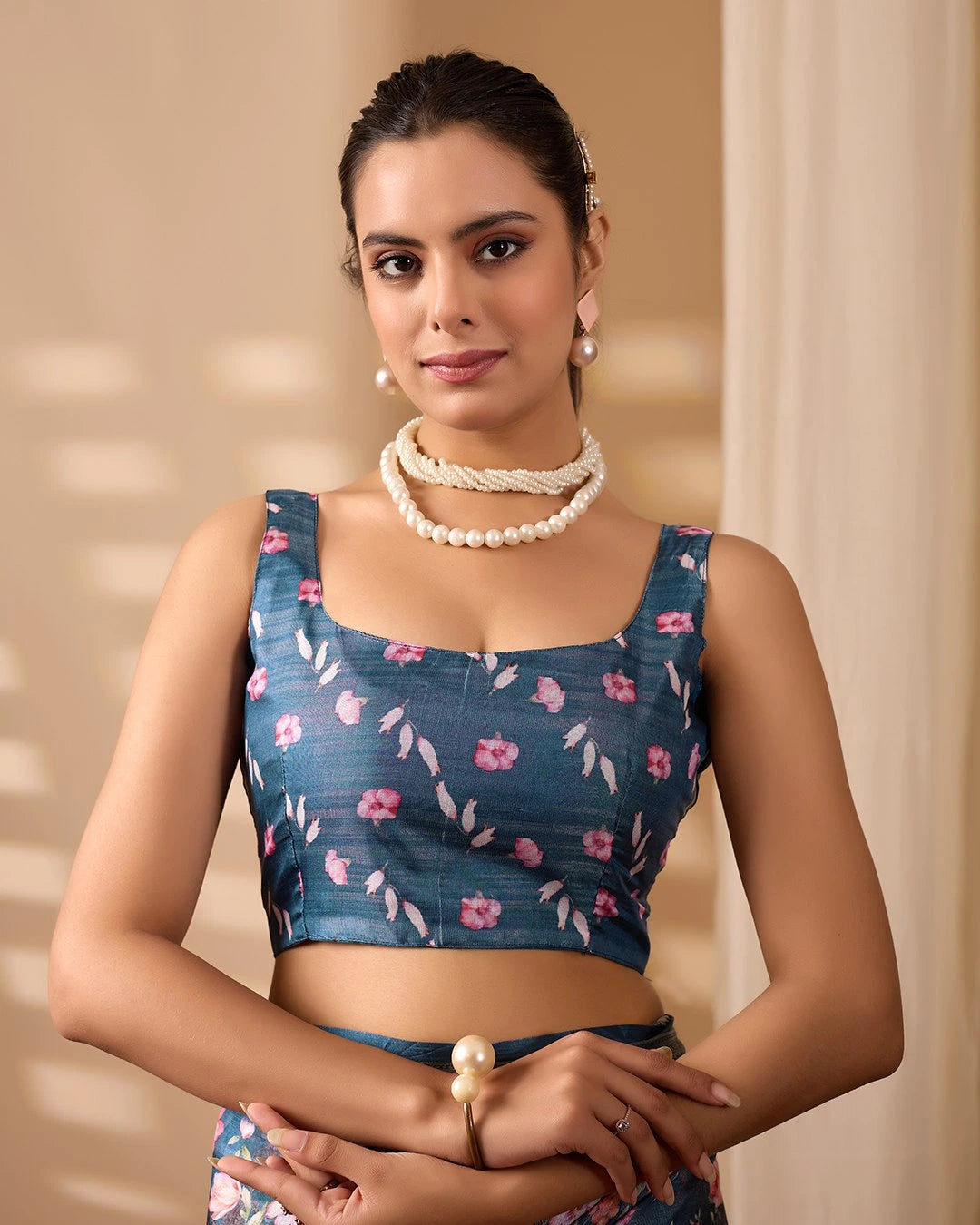 Woman wearing a blue floral blouse with a pearl necklace against a beige background