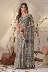 Woman wearing a patterned saree standing against a natural background with branches and rocks.
