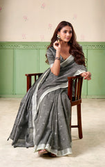 Woman in a gray saree sitting on a chair against a light green wall.