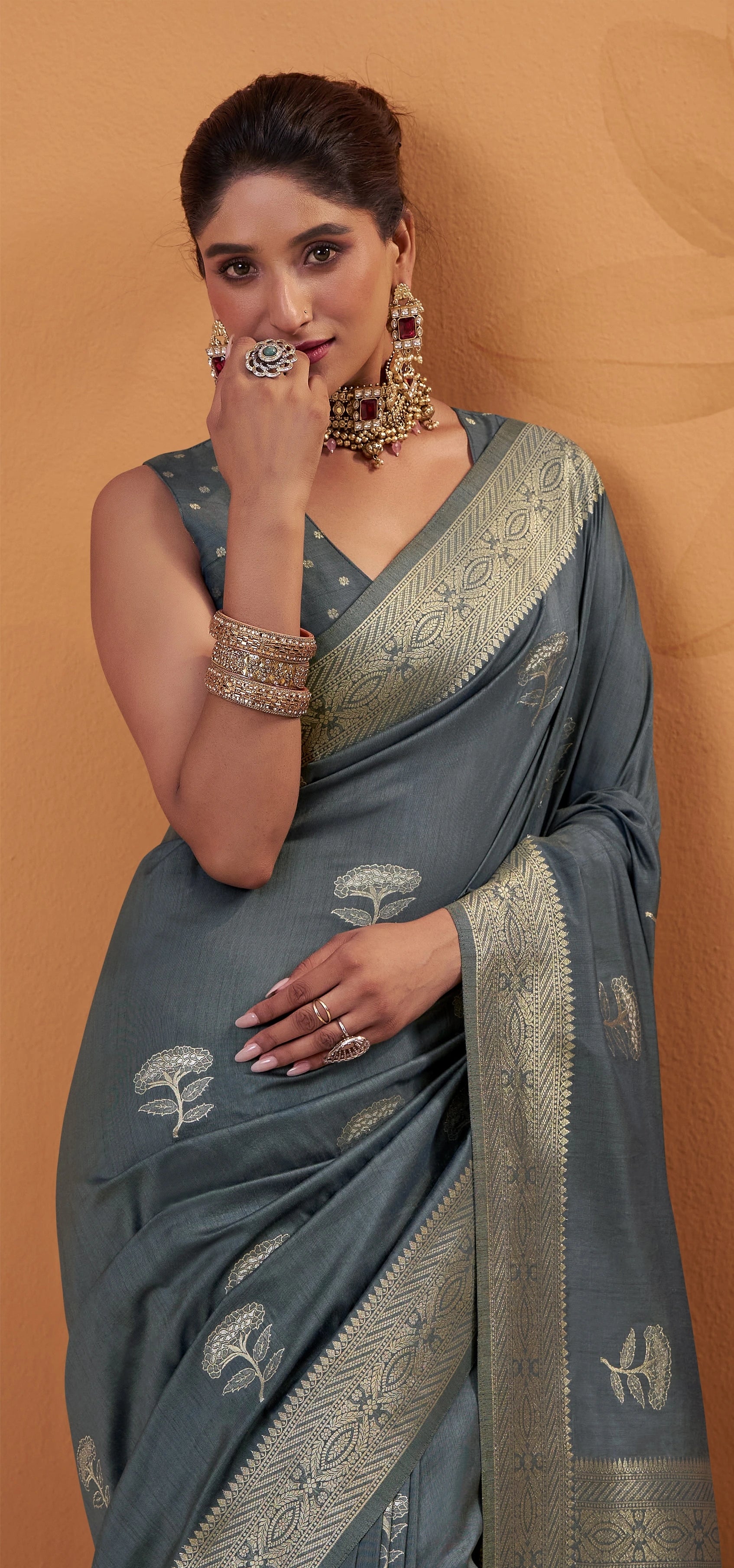 Woman wearing a gray saree with gold embroidery on a beige background