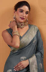 Woman in a gray saree with gold embroidery against a beige background