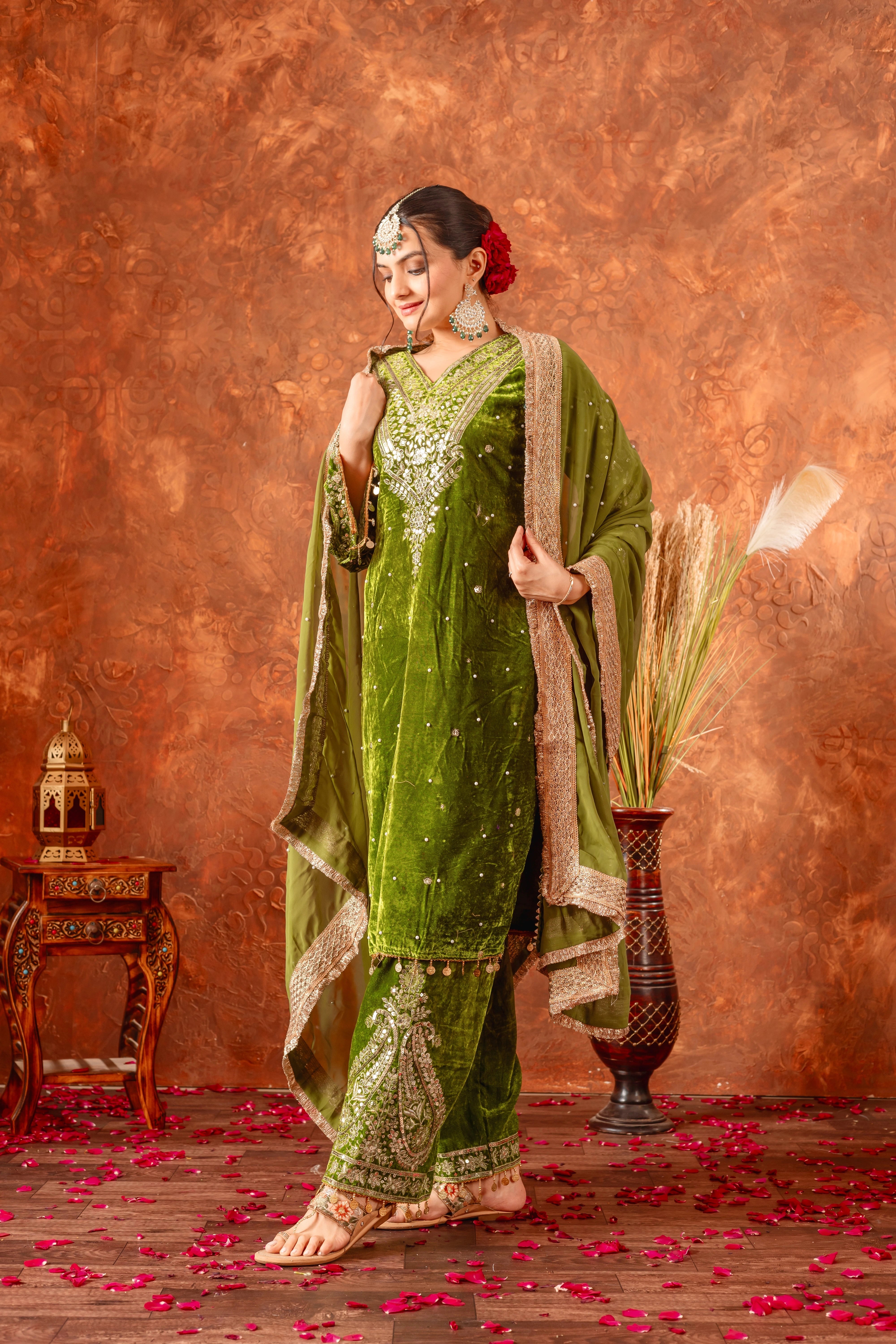 Woman in a green traditional outfit with gold embroidery against a textured brown background.