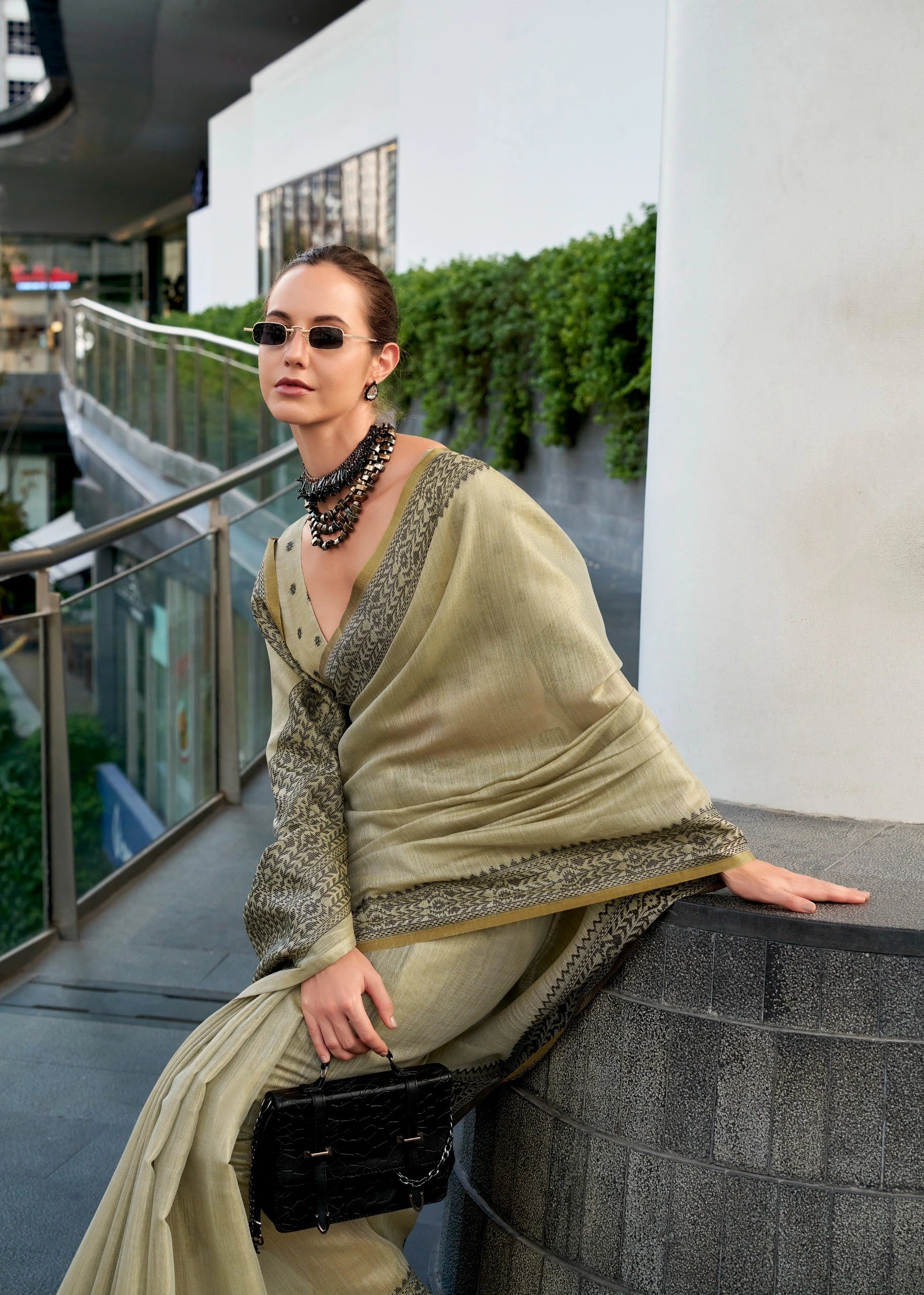 Woman in a light green traditional outfit with sunglasses and a black handbag on a balcony.