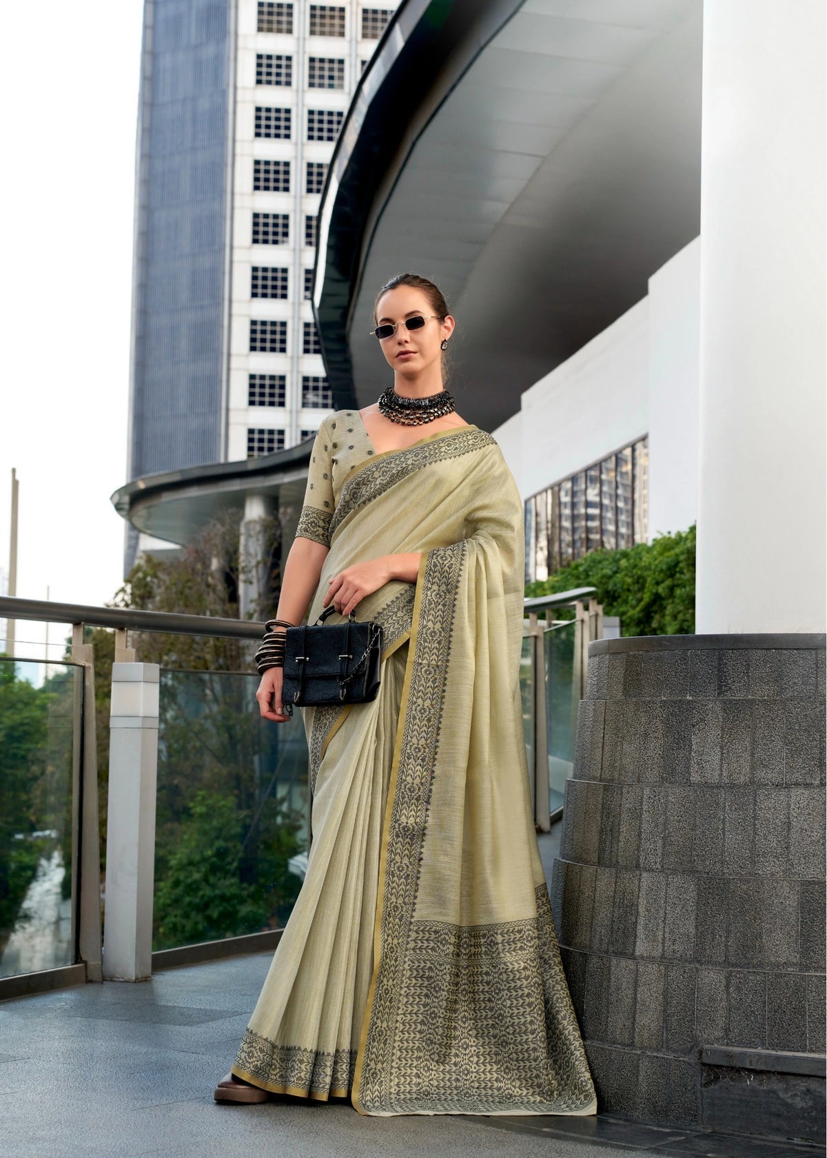 Woman in a saree standing in an urban setting with modern architecture.