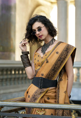 Woman in a mustard yellow saree with intricate patterns, standing outdoors.