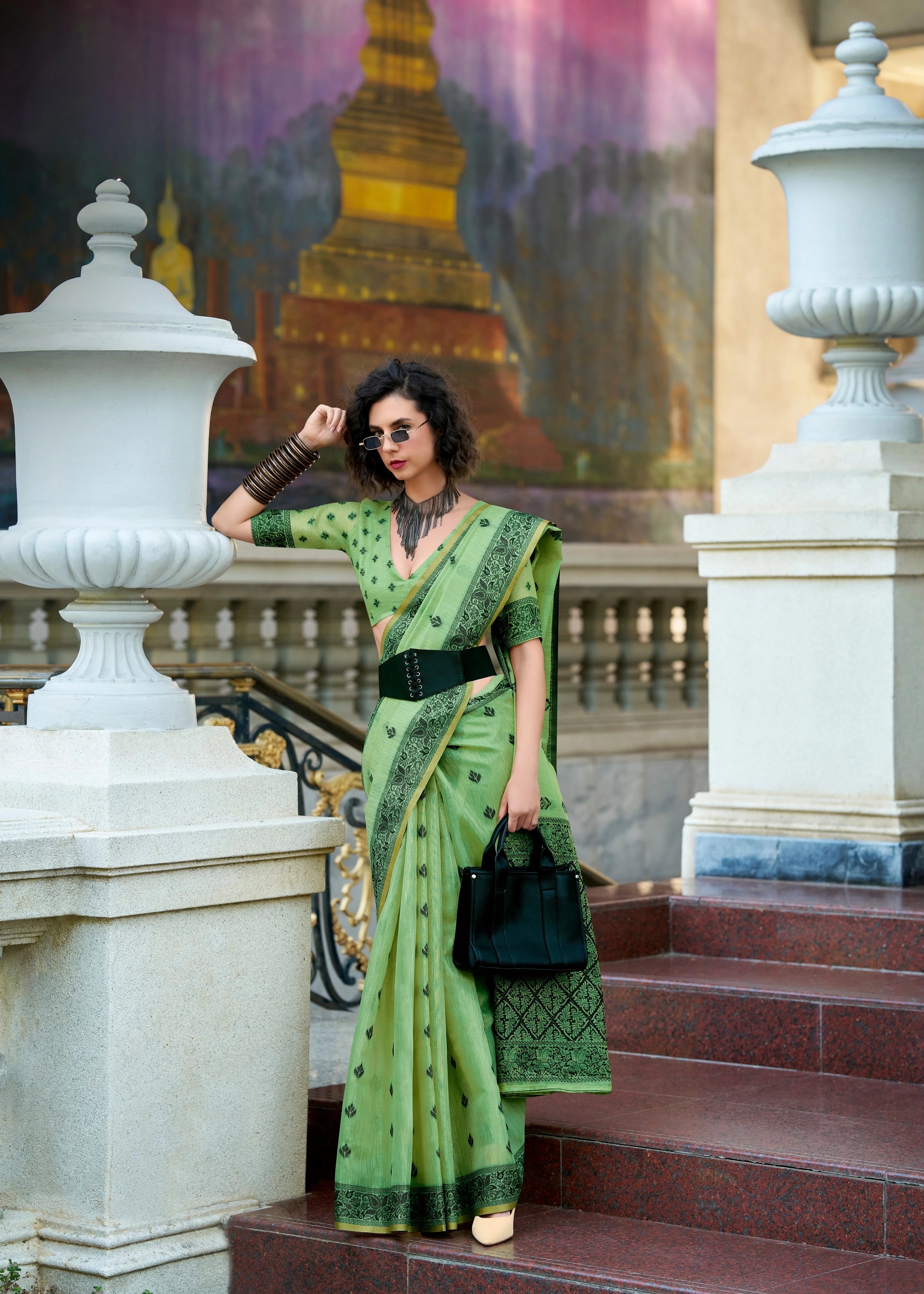Woman in a green saree standing on steps with classical architecture in the background