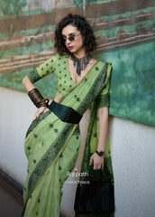 Woman wearing a green saree with black patterns against a textured wall.