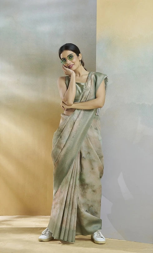 Woman in a light green saree standing against a neutral background