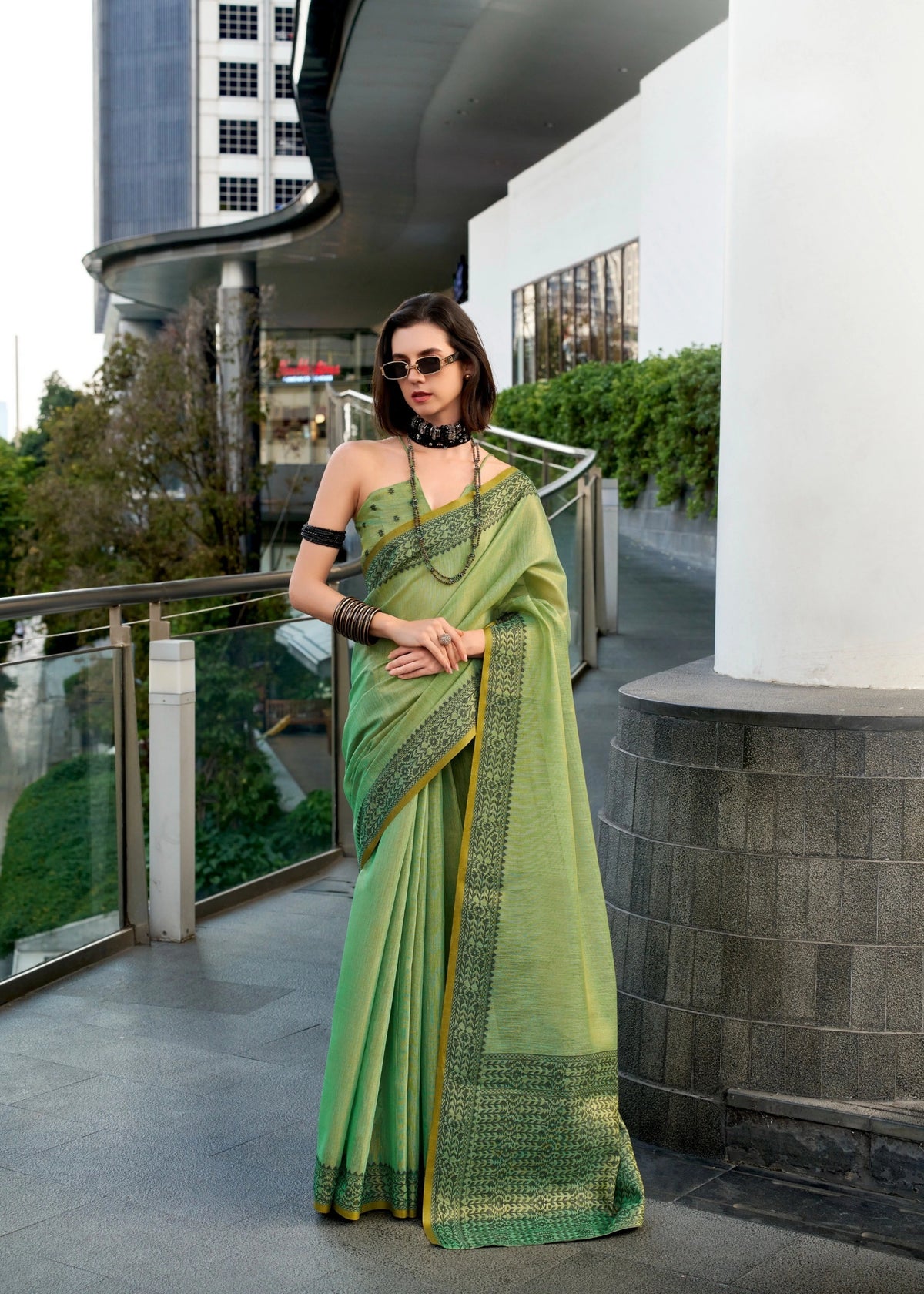 Woman in a green saree standing on a balcony with modern architecture in the background
