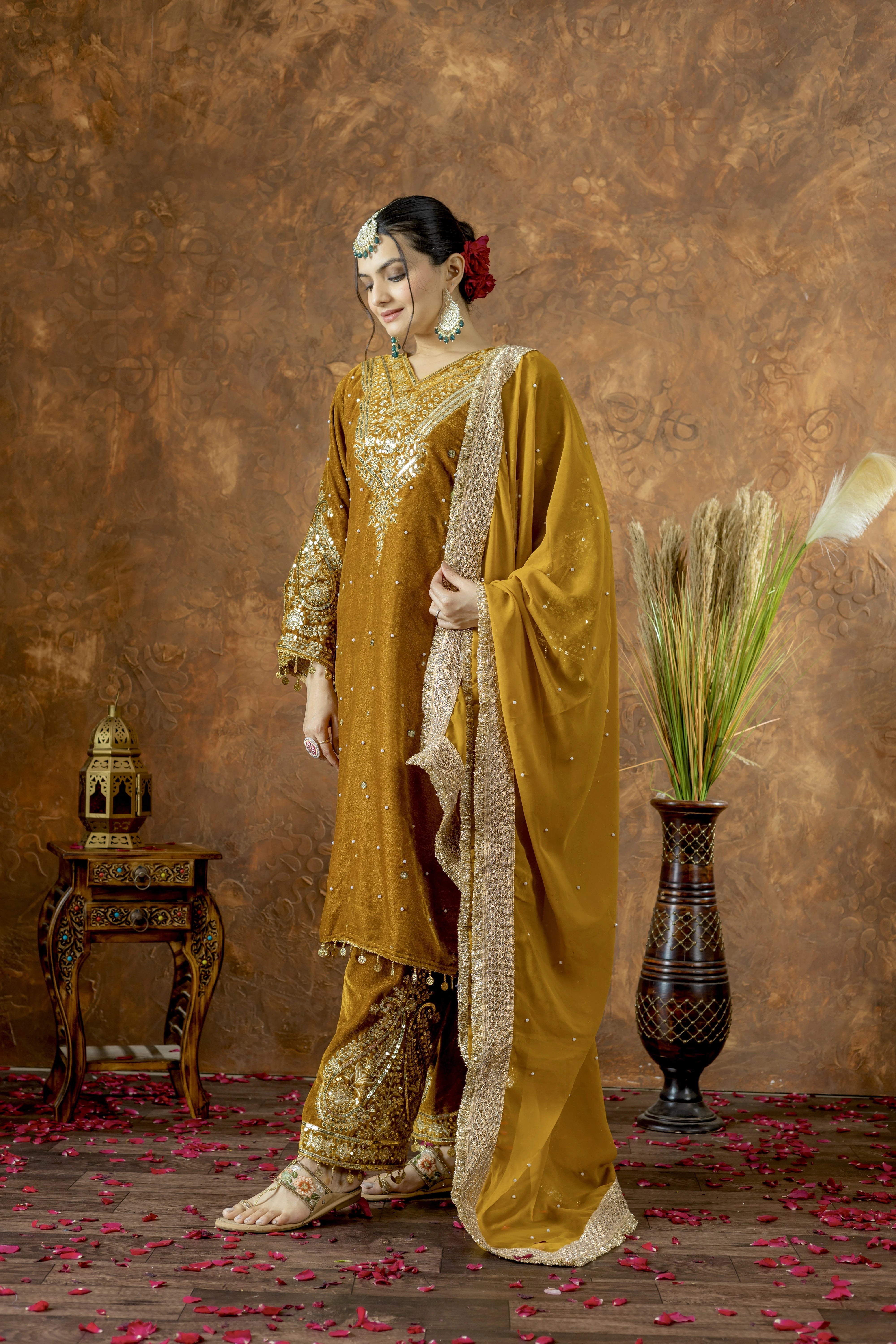 Woman in traditional mustard yellow and gold outfit with decorative elements on a brown background