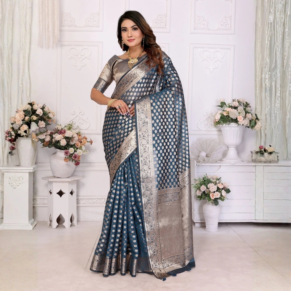 Woman in a blue saree with a white pattern standing in a decorated room with flowers.