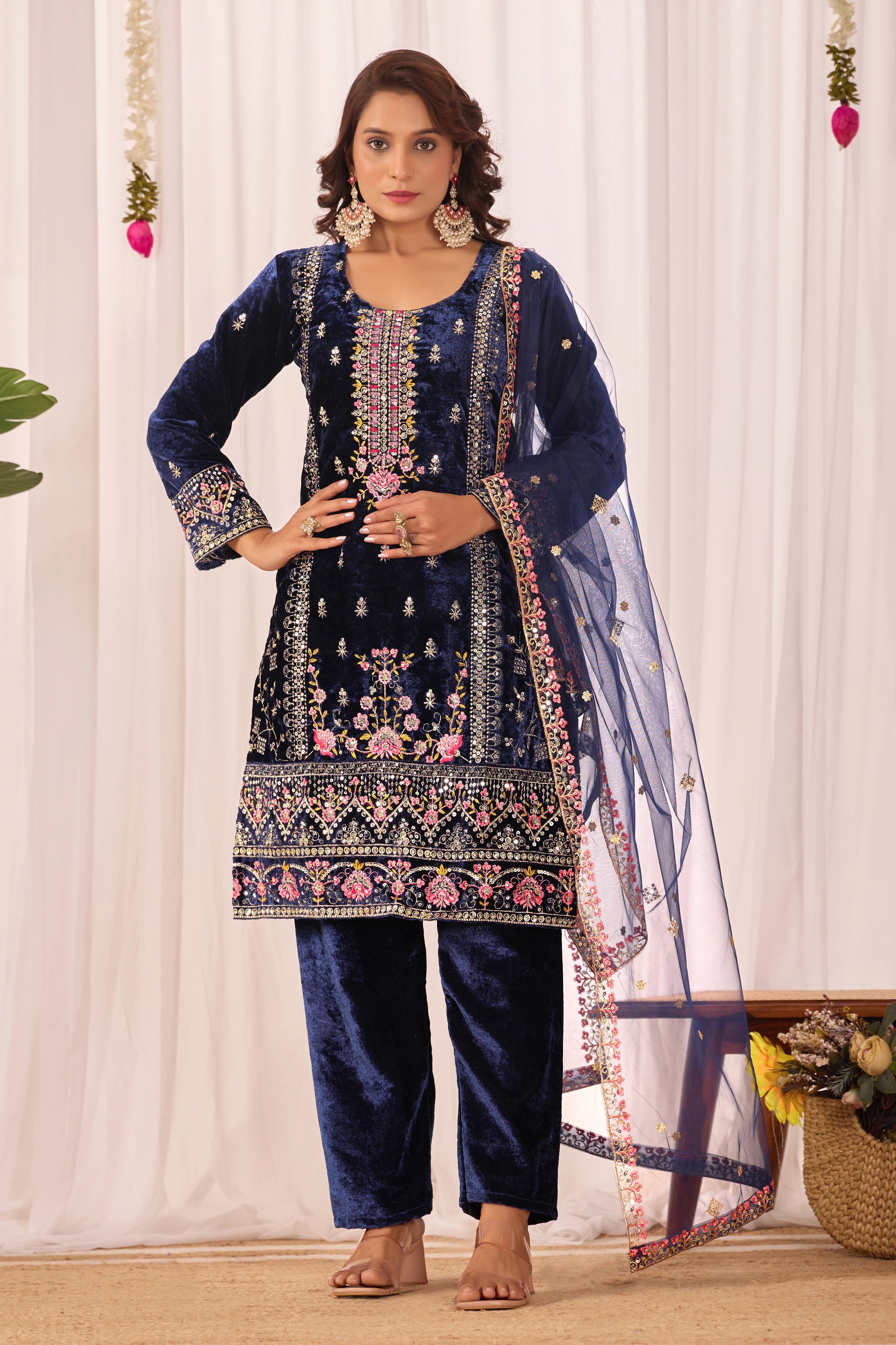 Woman wearing a navy blue embroidered traditional outfit with a white curtain background