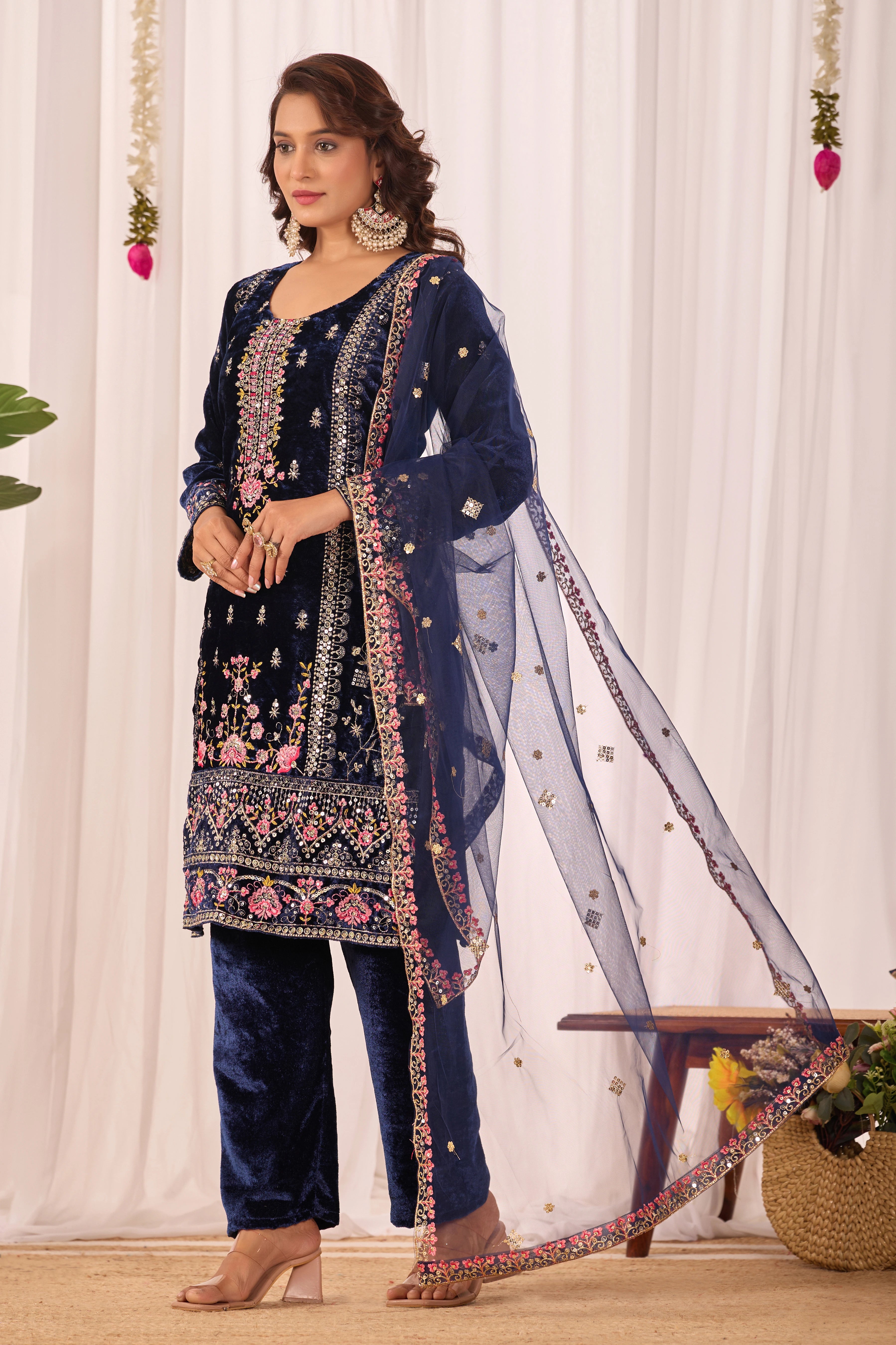 Woman wearing a navy blue embroidered outfit with a sheer dupatta against a white curtain background