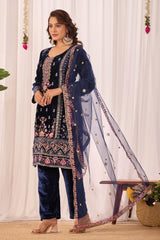 Woman wearing a navy blue embroidered outfit with a sheer dupatta against a white curtain background
