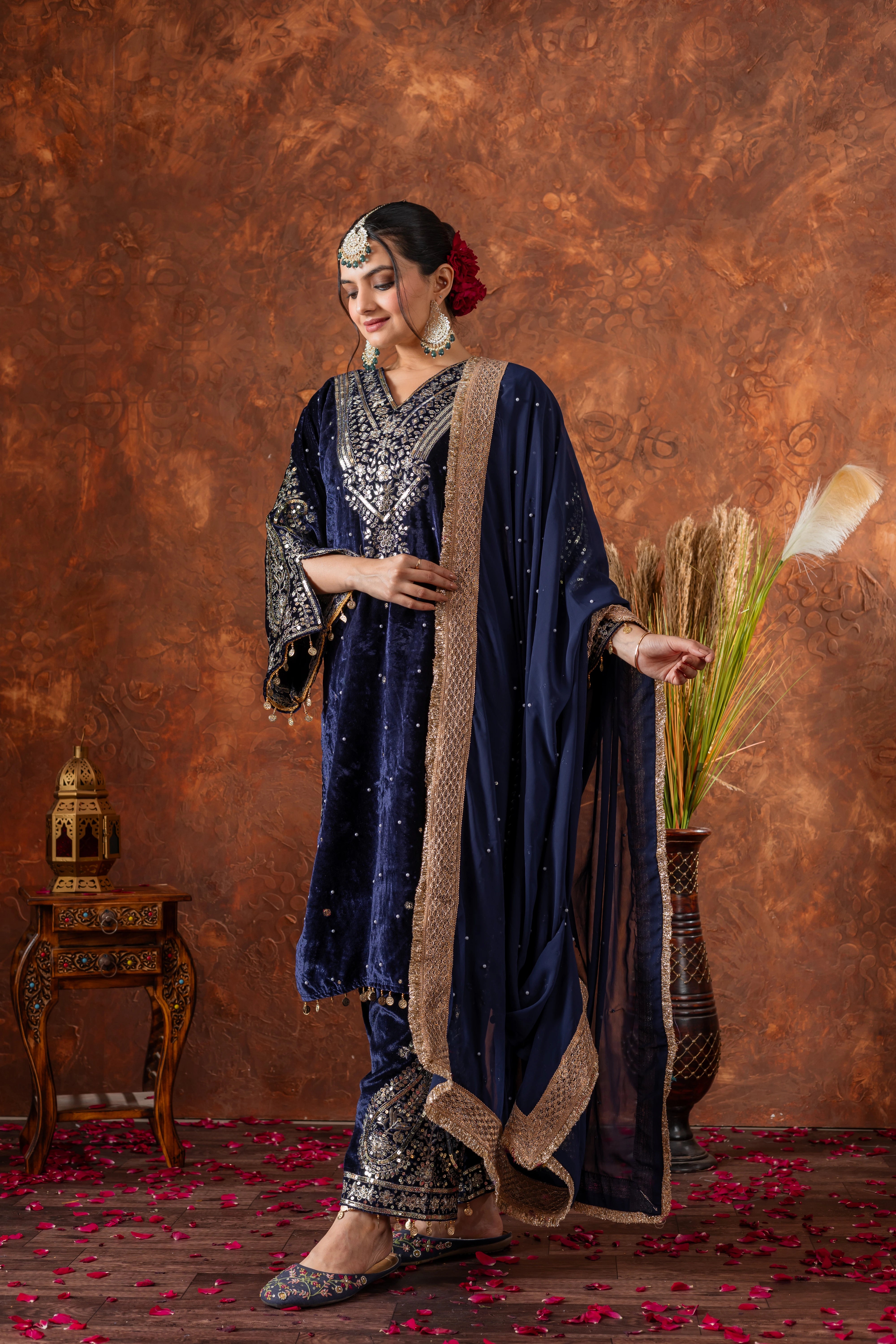 Woman in traditional blue and gold outfit with decorative accessories against a brown textured wall.
