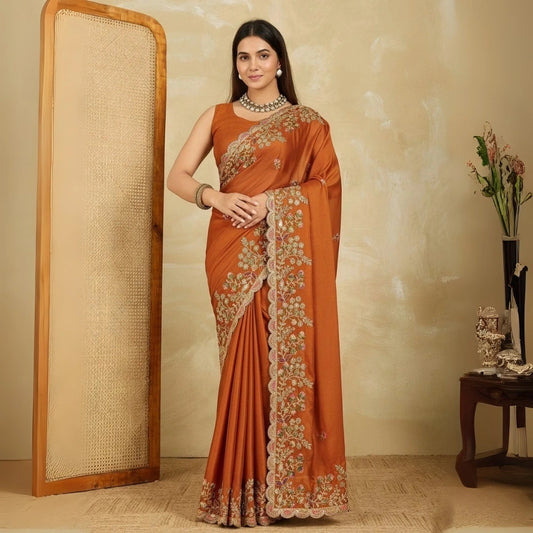 Woman wearing an orange saree with floral patterns in a room.
