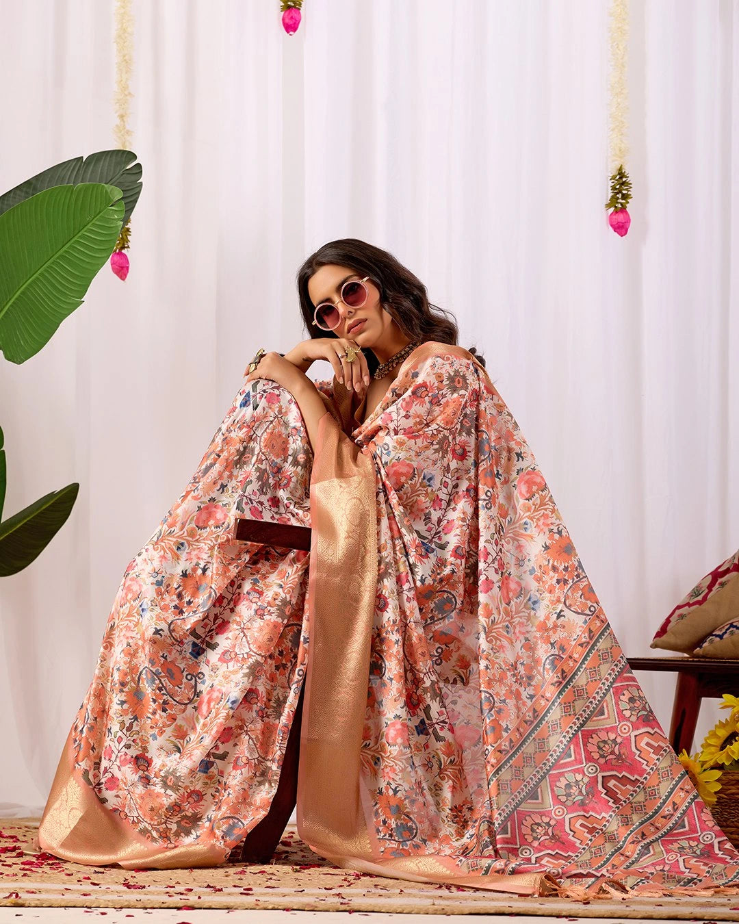 Woman wearing a floral saree with a white curtain background