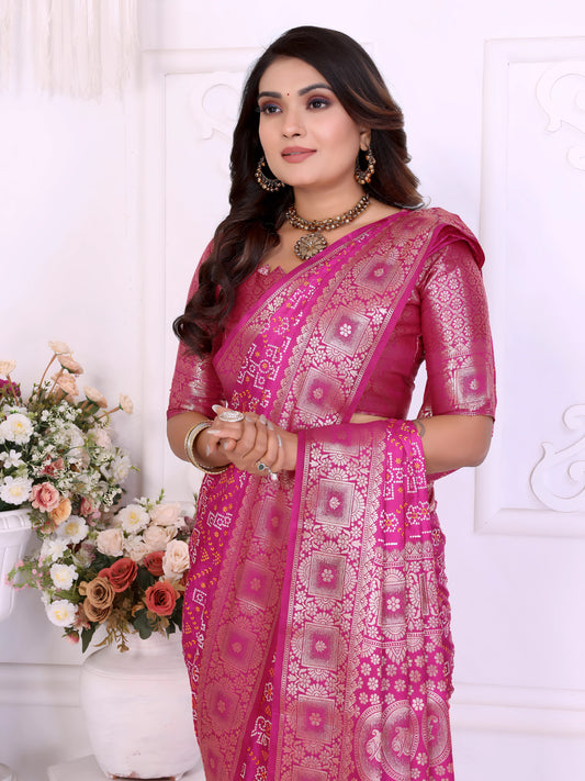 Woman wearing an elegant magenta Banarasi silk saree richly adorned with intricate zari motifs and a shimmering gold border, paired with a matching blouse and traditional jewelry. She poses gracefully in a classic white room decorated with ornate wall panels and vases overflowing with pastel and rose-colored artificial flowers.