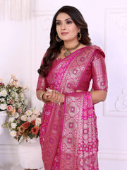 Woman wearing an elegant magenta Banarasi silk saree richly adorned with intricate zari motifs and a shimmering gold border, paired with a matching blouse and traditional jewelry. She poses gracefully in a classic white room decorated with ornate wall panels and vases overflowing with pastel and rose-colored artificial flowers.