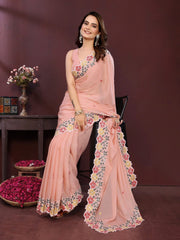 Woman wearing a pink saree with floral patterns sitting on a chair against a dark background.