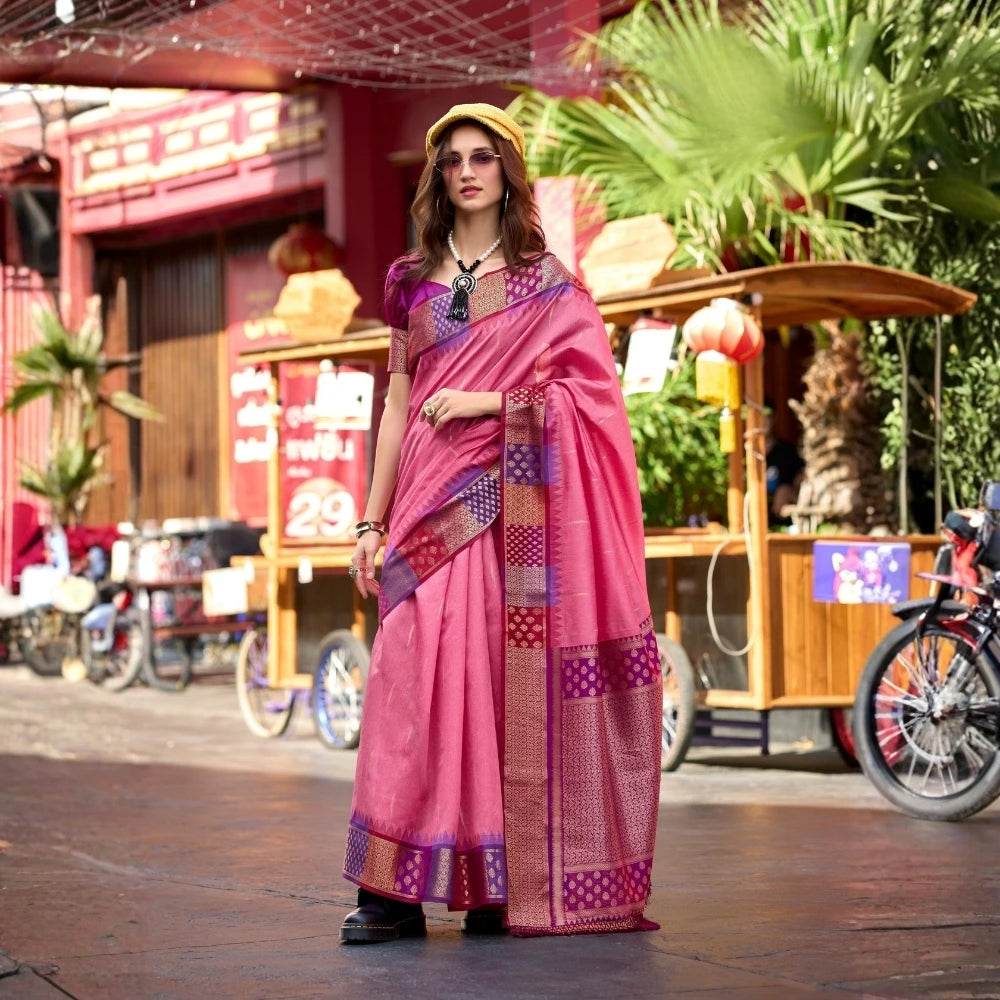 Woman in a pink saree with a colorful pattern standing on a street.
