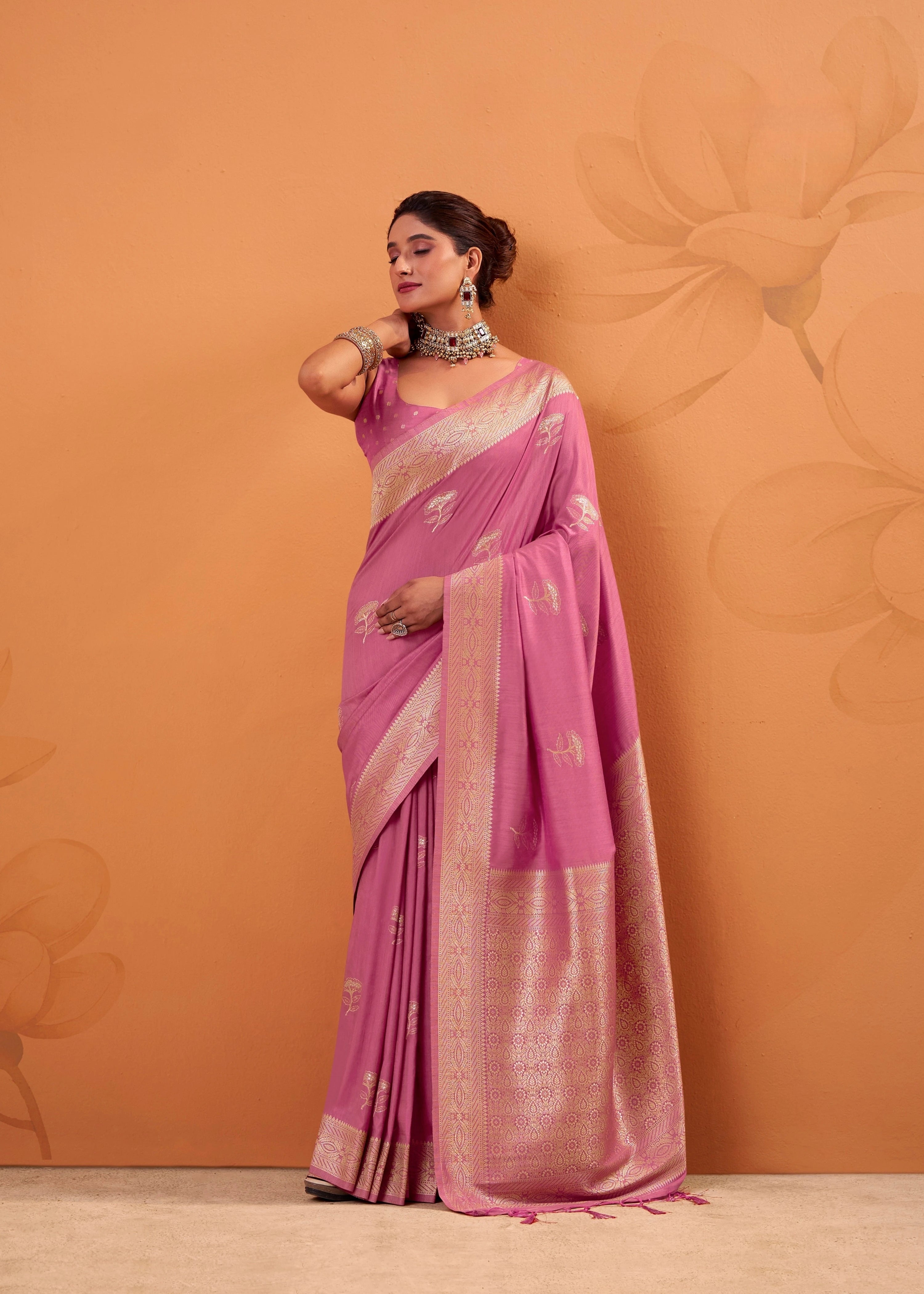 Woman wearing a pink saree with a floral pattern against an orange background