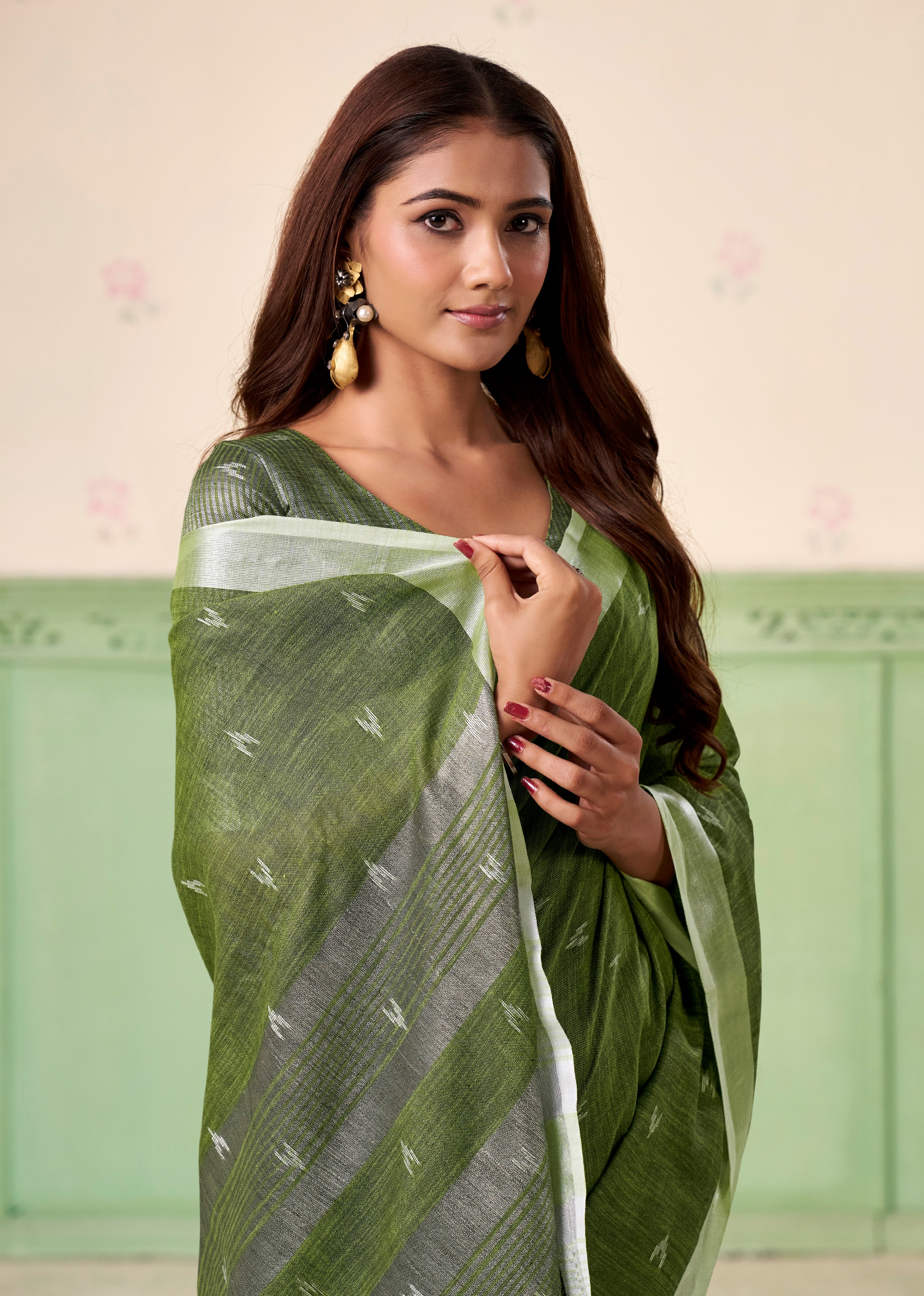 Woman wearing a green saree with a white border against a light background