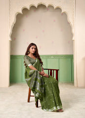 Woman in a green saree sitting in a decorated room with an archway.