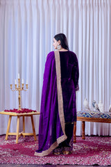 Woman in a purple traditional outfit standing in a decorated room with white curtains and floral arrangements.