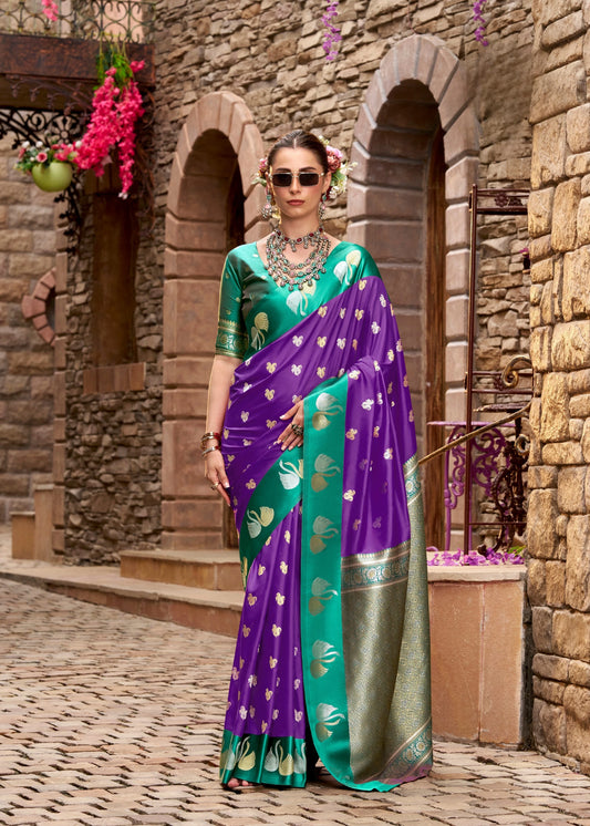Woman in a purple and green saree standing in front of stone arches.
