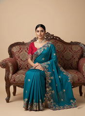 Woman in a blue saree sitting on an ornate couch with a beige background