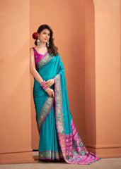 Woman wearing a teal and pink saree against a beige wall