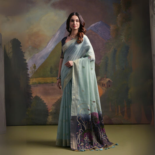 A woman models a soft Sea Green Muga Silk Saree with subtle Resham weaving. The pallu dramatically transitions to a deep indigo/black color, featuring intricate purple and green floral Resham threadwork. She wears a dark blouse and an oxidized silver choker necklace.