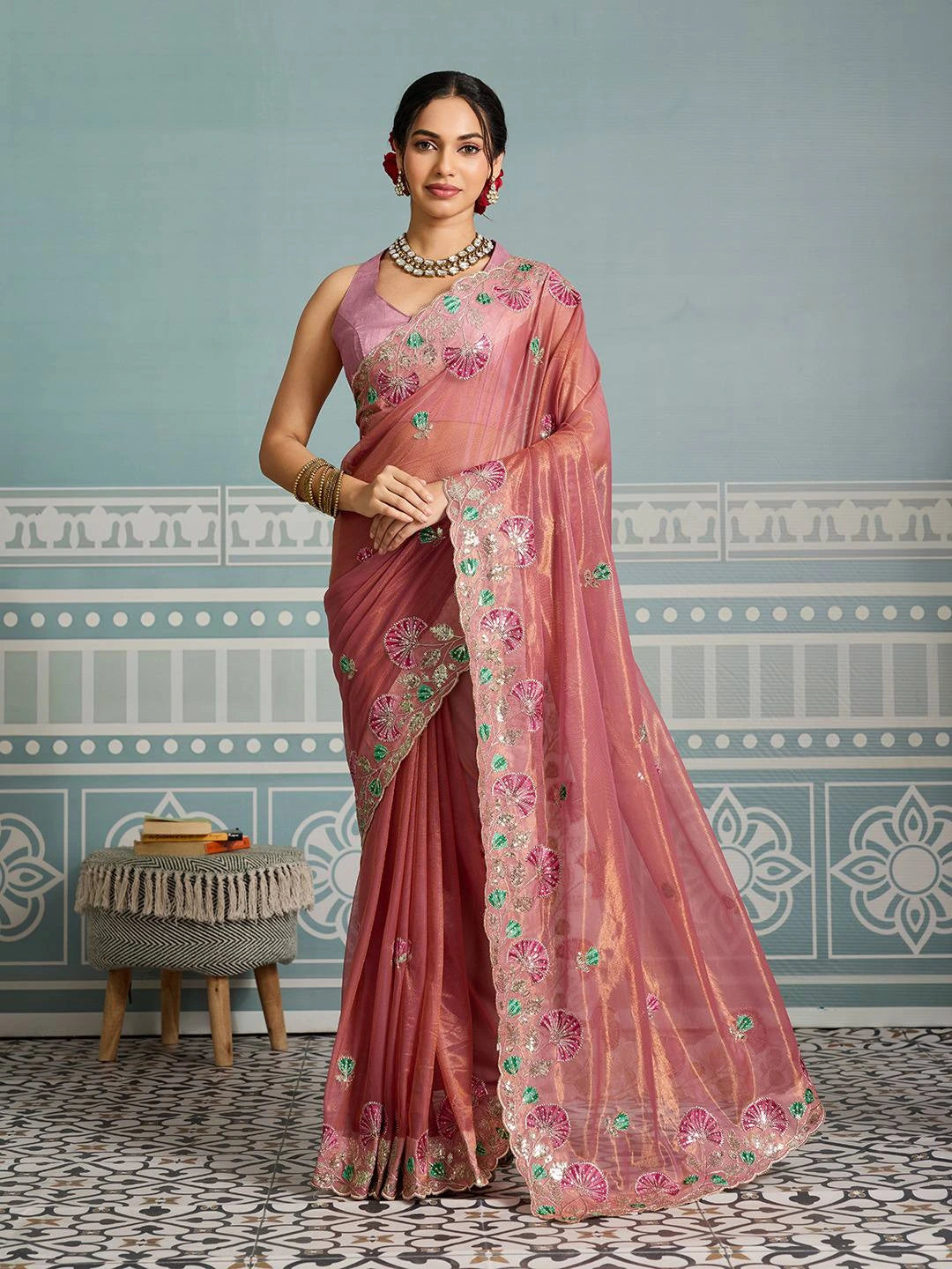 Woman wearing a pink saree with floral patterns in a room with decorative walls.