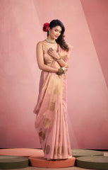 Woman in a light pink saree with gold patterns on a pink background