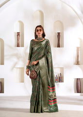 Woman in a green saree with red patterns standing in a white interior setting.