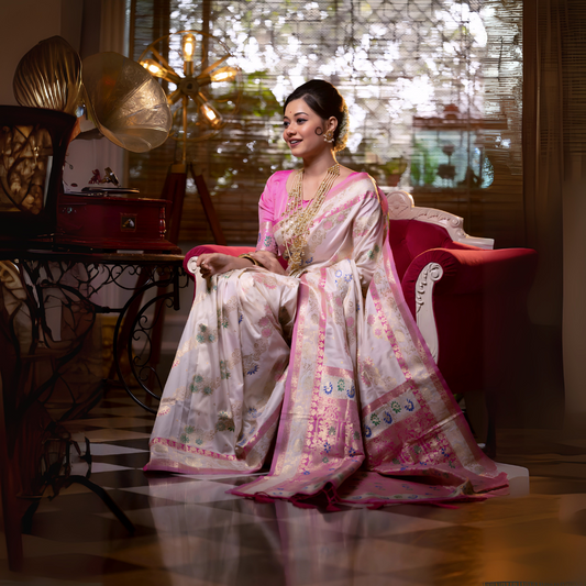 Woman wearing an ivory Banarasi silk saree with intricate pink floral zari border and pallu, paired with a pink blouse and layered gold jewelry, seated on a vintage white and red sofa in an elegant room with a gramophone, wooden blinds, and patterned flooring.

Related
File name: modern-minimalist-architecture
Alt text: Sleek modern minimalist architecture with clean lines and large glass windows.