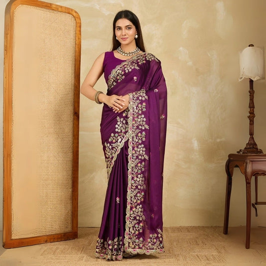 Woman in a purple saree with gold embroidery standing in a room.