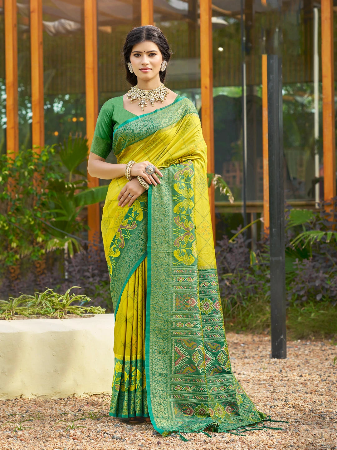 Woman wearing a green and yellow saree with a patterned border outdoors.
