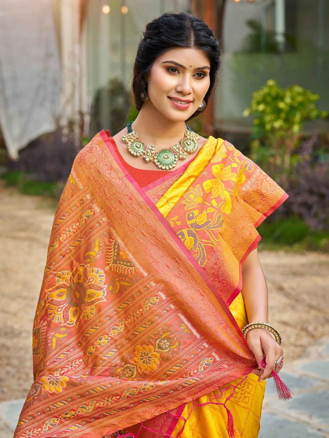 Woman wearing a traditional orange and yellow saree with a blurred outdoor background