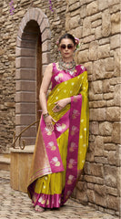 Woman in a yellow and pink saree standing against a stone wall.