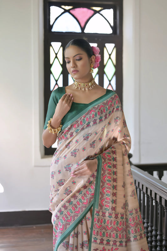 Woman wearing a beige block print saree with a green border and matching green blouse, accessorized with a choker necklace and floral hair accessory, standing in a sunlit vintage interior beside a stained glass window and dark wooden railing.