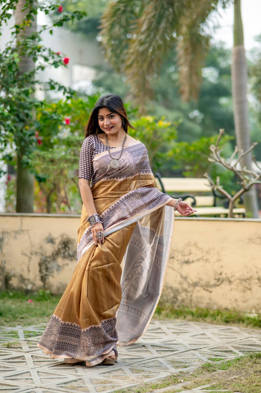 Woman in a beige saree with Madhubani print standing near a pond with lotus flowers in a lush garden setting